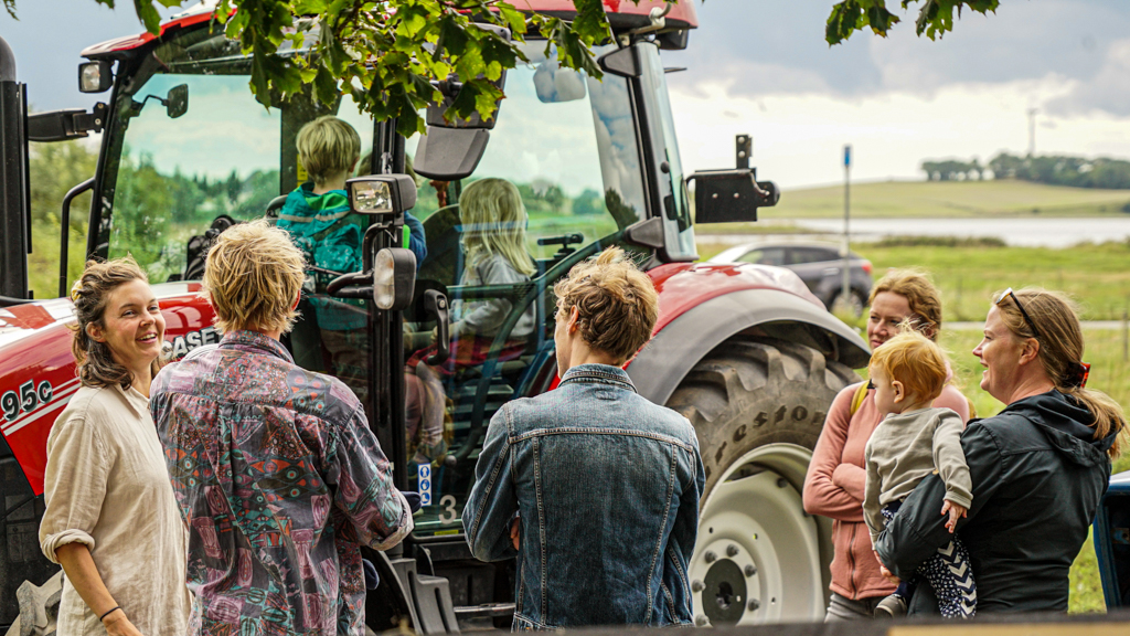 Voksne står og taler, mens deres børn leger på en traktor